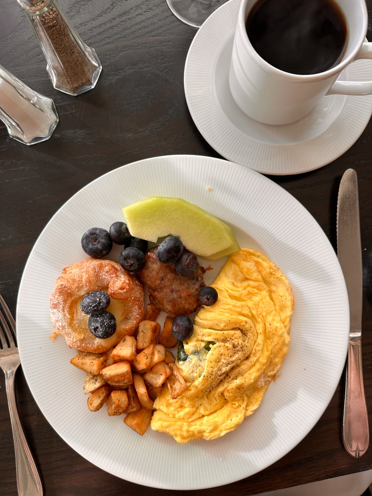 overhead shot of breakfast plate of omelet, melon, hashbrowns, blueberries, and black coffee