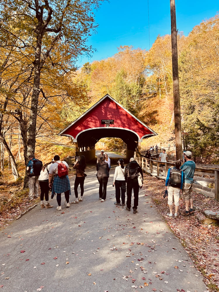 a group of tourists waiting to get a photo in front of a red covered bridge at The Flume