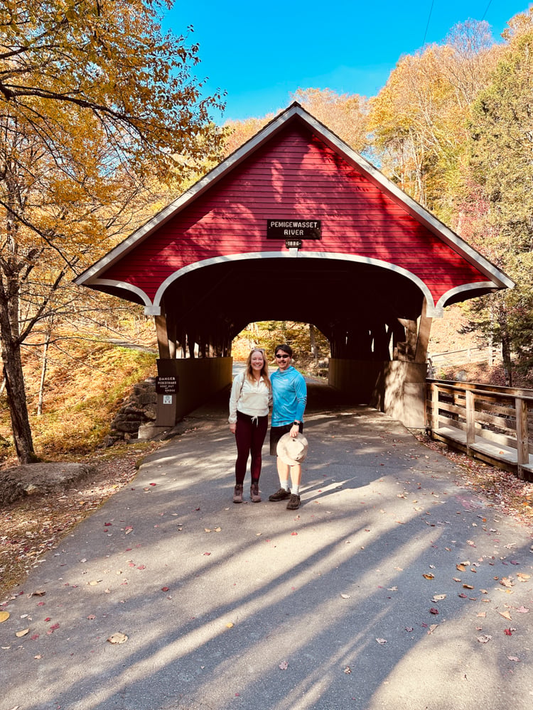 Rachelle and Pete under a red covered bridge during a New Hampshire fall foliage road trip