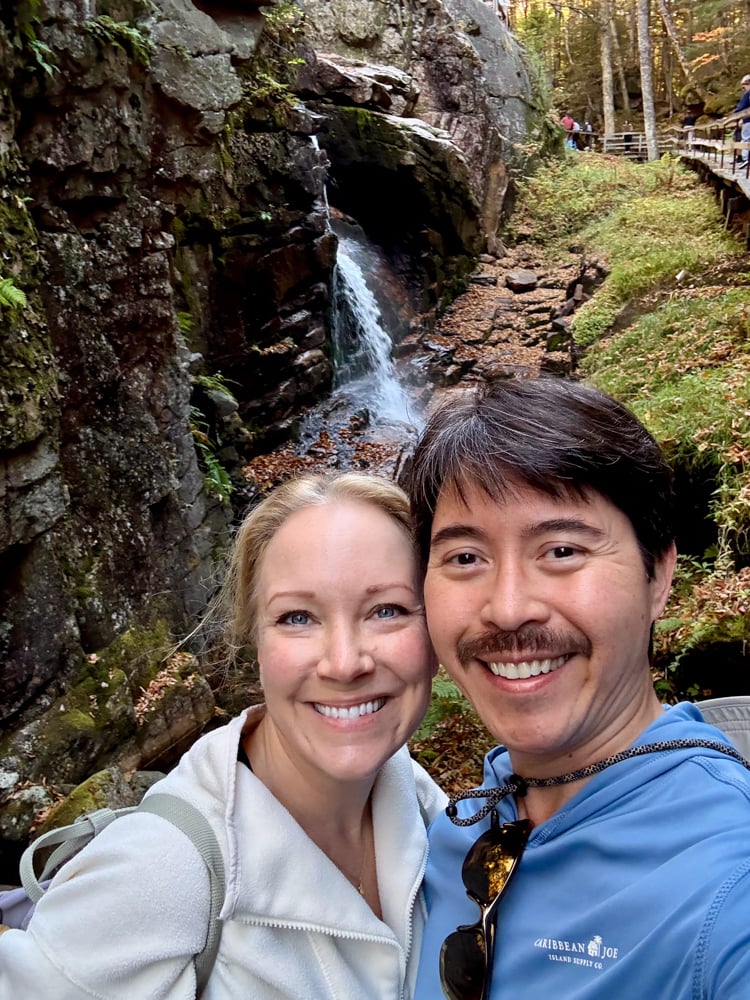 Rachelle and Pete taking a selfie in front of the top of the waterfall of The Flume in New Hampshire