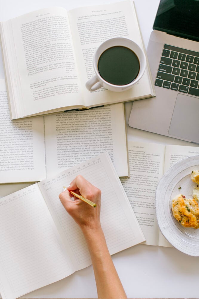 Book open with coffee on top and a hand taking notes