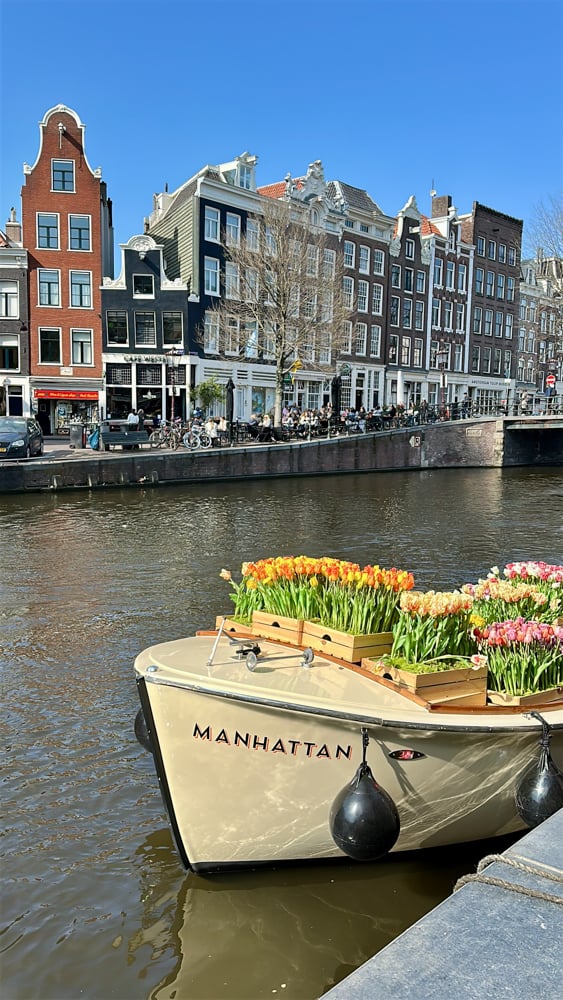 Historic canal houses along an Amsterdam canal with a boat filled with tulips